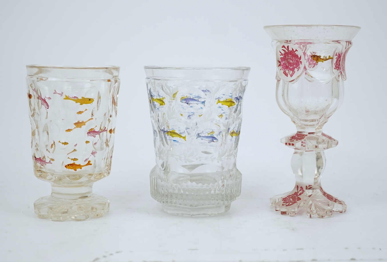 Two Bohemian transparent enamelled ‘fish’ beakers, and a similar faceted goblet, c.1840-60